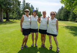 Cuatro mujeres paradas en un campo de golf usando camisetas blancas que combinan.