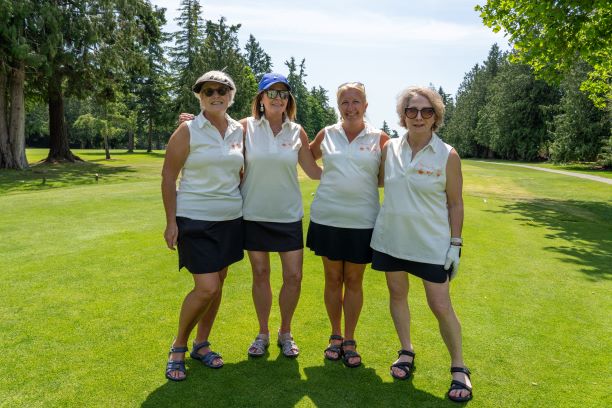 Cuatro mujeres paradas en un campo de golf usando camisetas blancas que combinan.