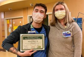 Simeon Billick sostiene el certificado del premio DAISY Award y posa junto a una mujer.
