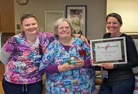 Tres mujeres posan juntas con el premio y el certificado del Rose Award.