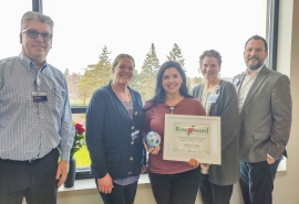 A group of five pose together for photo. Addie Carlson, Rose Award winner, stands in the middle holding her award and certificate.