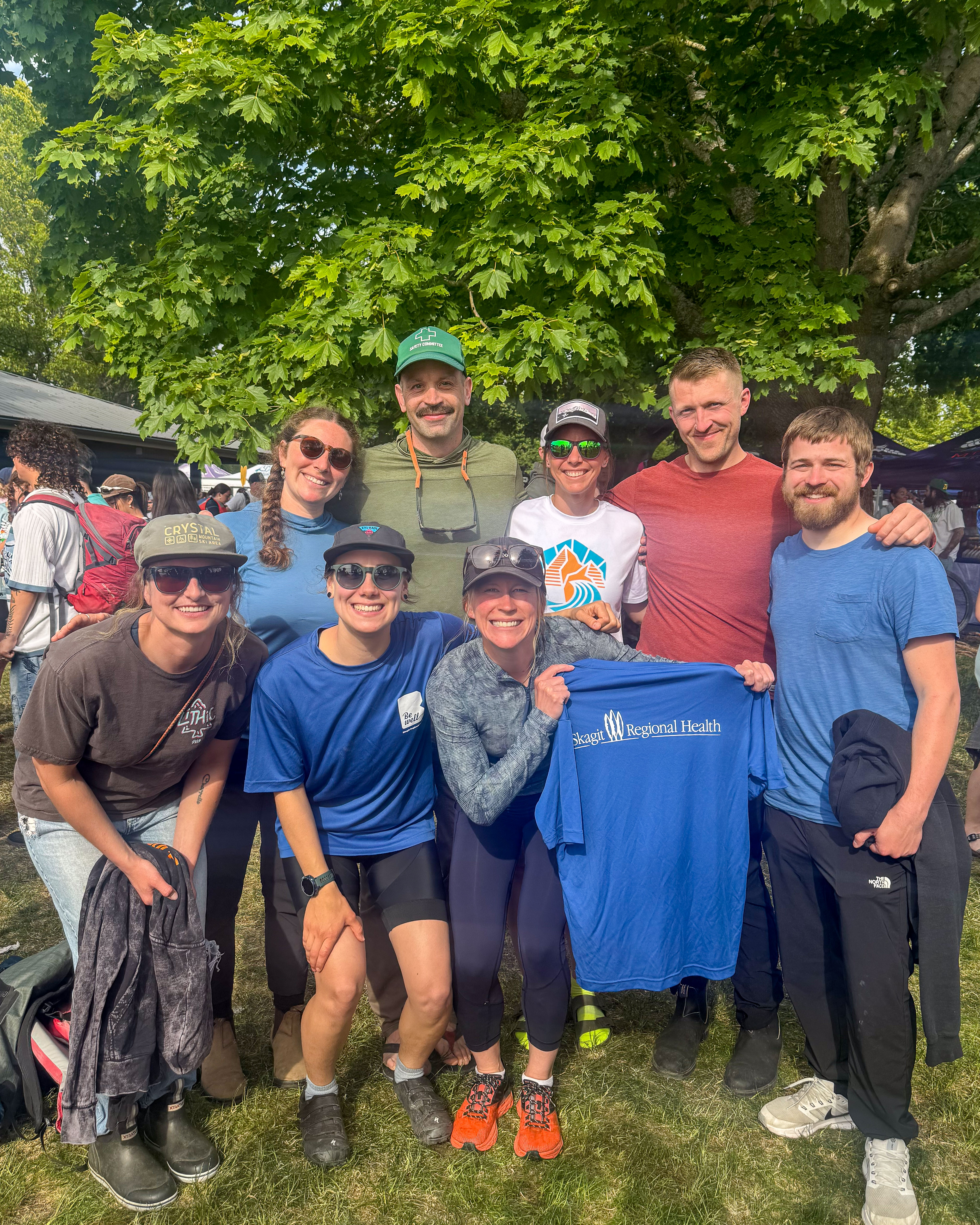 Group of eight stands together holding up blue Skagit Regional Health shirt.