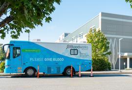 Large blue and white bus is parked outside a facility.