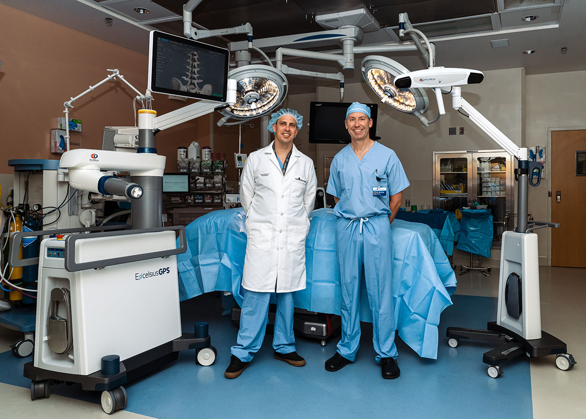 Cirujanos de columna parados en el quirófano junto a la mesa de operaciones con un nuevo robot quirúrgico.