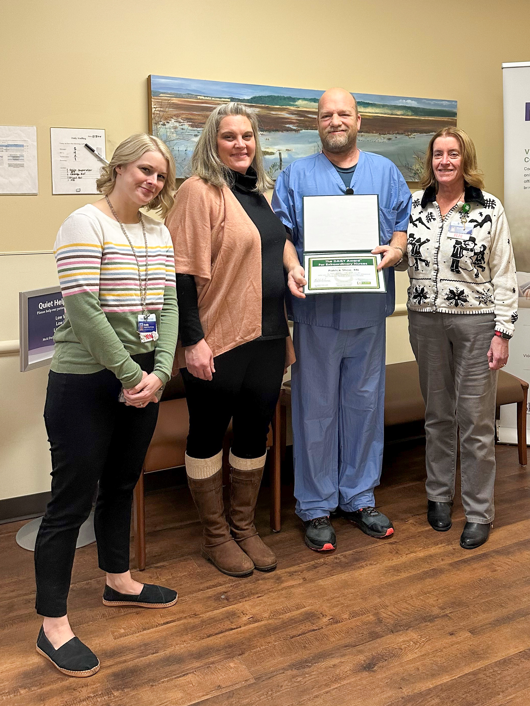Four Cascade Valley Hospital staff members stand together, one male in scrubs holds the DAISY Award certificate.
