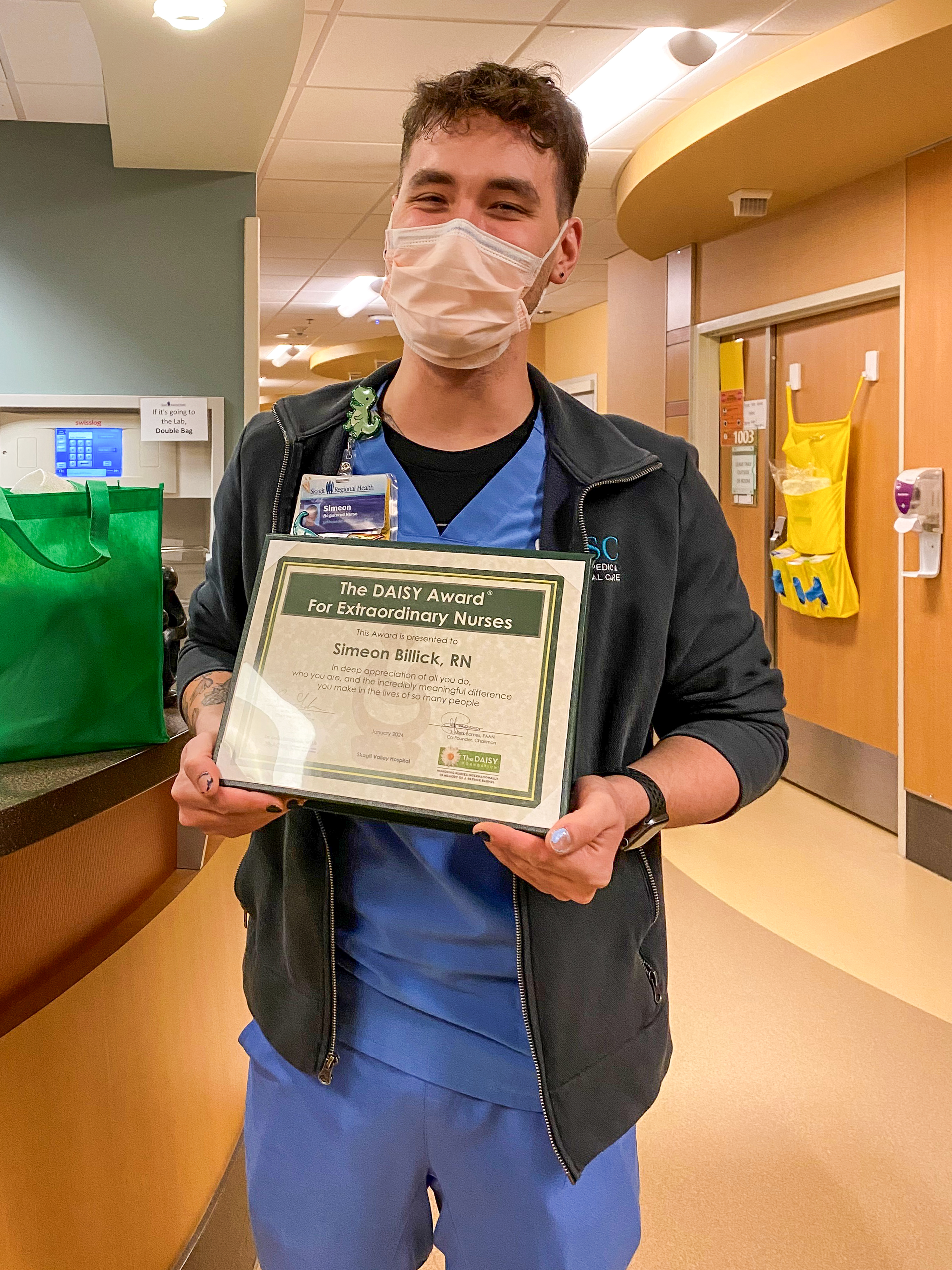 Simeon Billick, RN sonríe mientras sostiene el certificado de su DAISY Award.