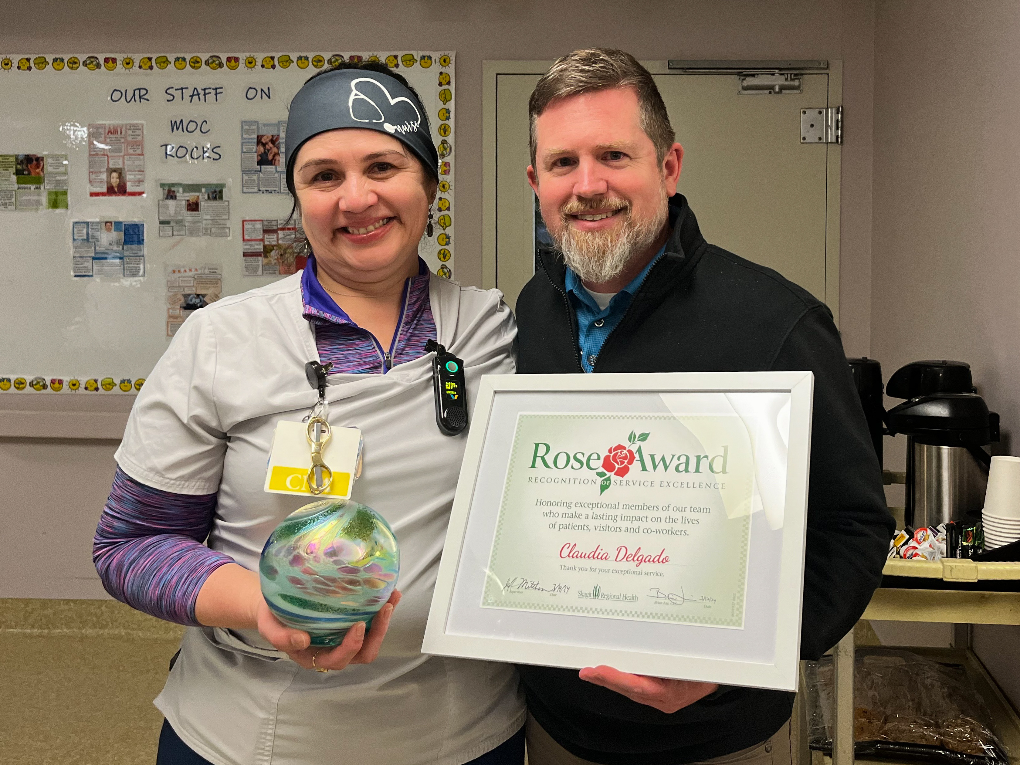 Woman, left, holds a glass globe and poses next to man, right, who holds the framed Rose Award certificate.