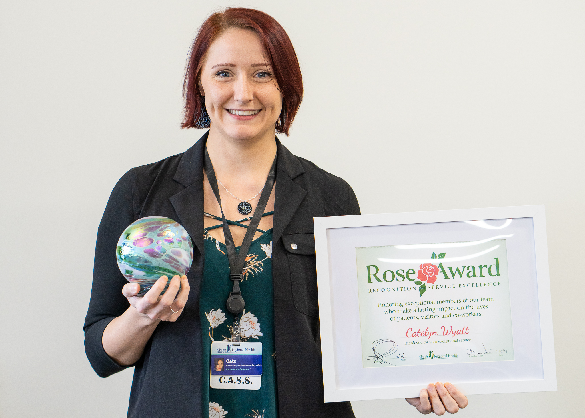 Woman holds glass blown art and Rose Award certificate and smiles for camera. 