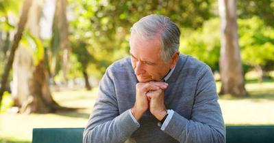 Depression, thinking and senior man in garden sitting on bench for fresh air in nature.
