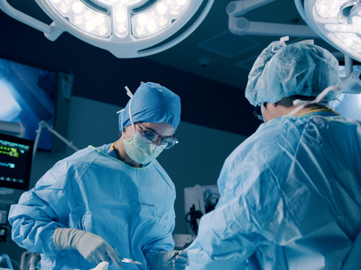 Una cirujana mira hacia abajo, hacia la mesa de operaciones en un quirófano, durante un procedimiento.