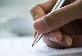 una mano sosteniendo una pluma para escribir sobre un papel