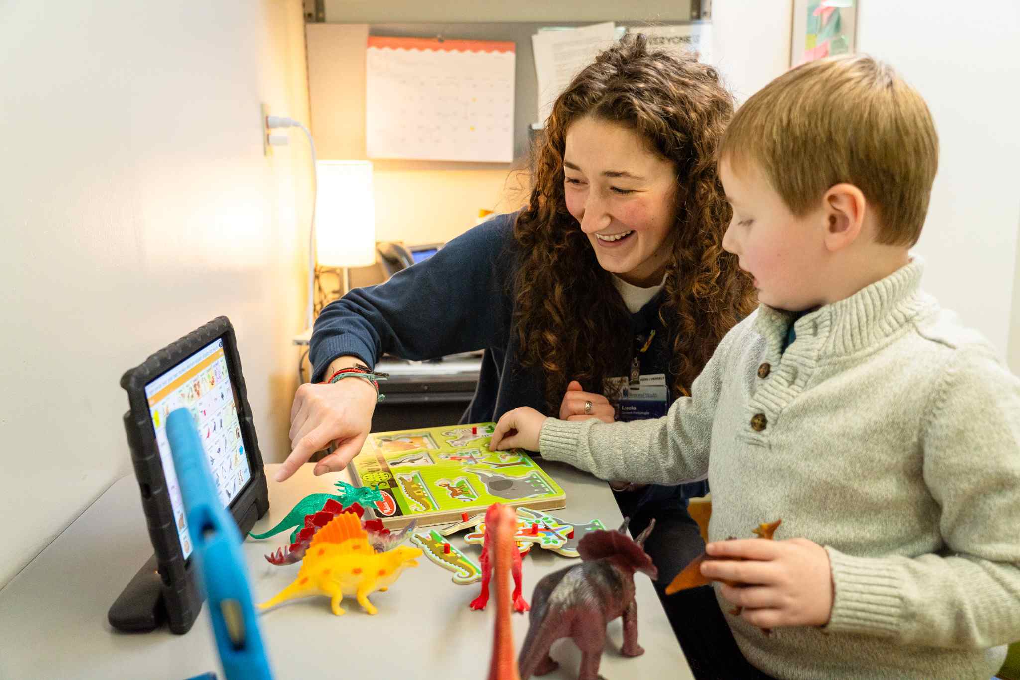 Child playing with toys at a desk with an adult using an educational tablet