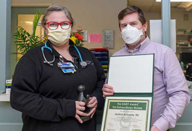 Female nurse poses holding Healer's Touch statue, standing next to male holding DAISY award certificate.