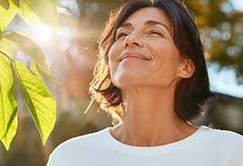 Mujer parada al sol cerca de unas hojas