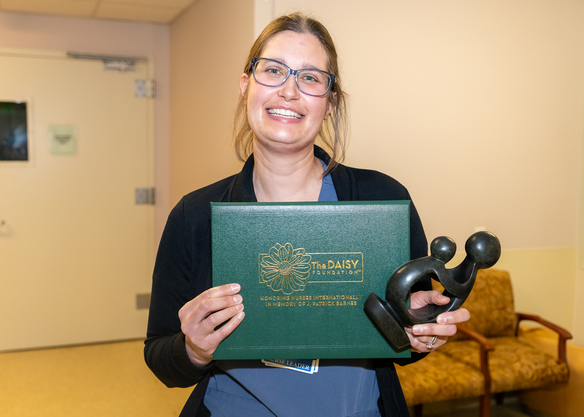 Jessica Thompson, RN, holds DAISY Award certificate and Healer's Touch statue.