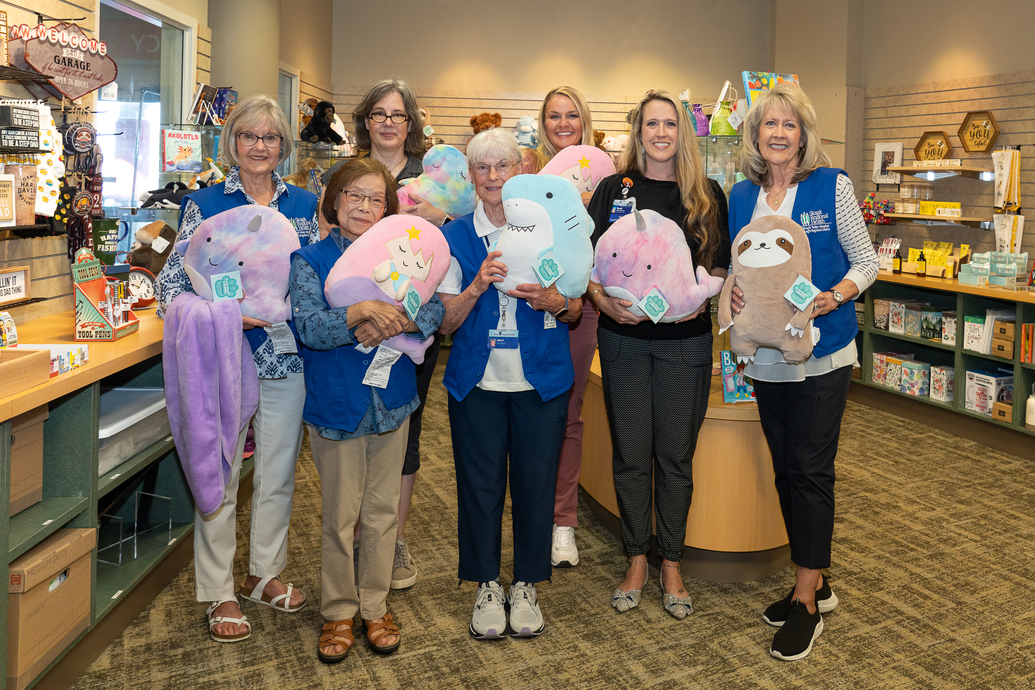 Four volunteers and three nurses hold colorful stuffed animals while standing inside the Gift Shop at Skagit Valley Hospital.