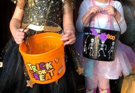 Dos niñas disfrazadas sostienen recipientes para pedir dulces.