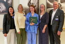Group of five people smile at the camera. There is a female nurse in the middle, holding a DAISY Award certificate and Healer's Touch statue.