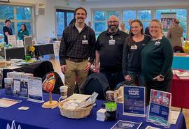Four people stand behind a Skagit Regional Health table at a community health fair, with brochures and health materials displayed.