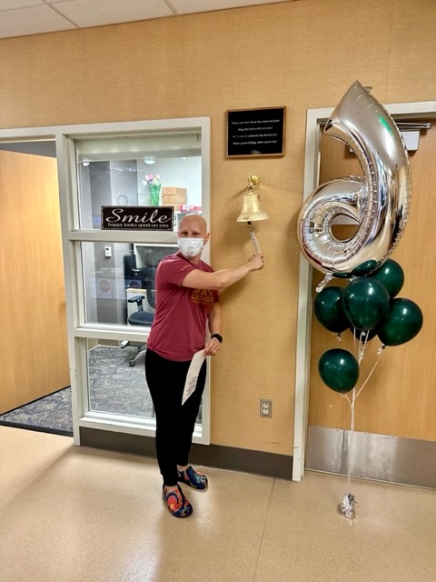 Woman in red t shirt rings bell with right arm, balloons pictured to right of woman.