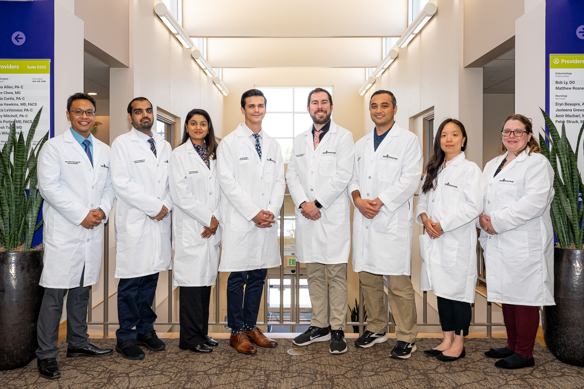 Eight residents in white coats stand shoulder to shoulder.