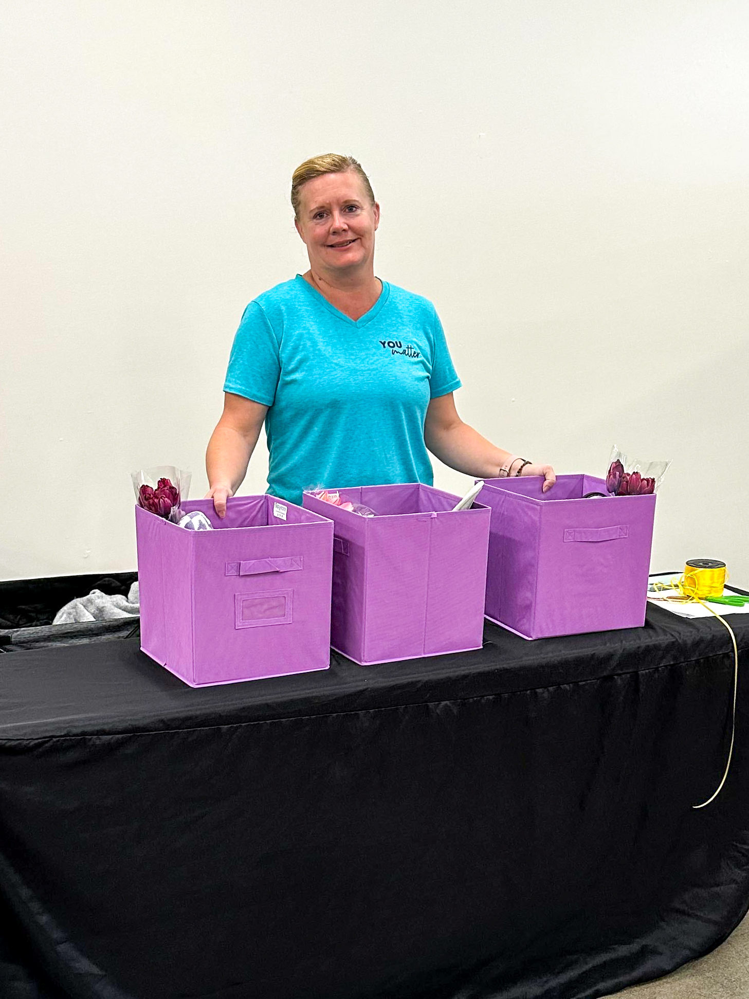 Woman in blue t-shirt poses behind three purple storage boxes. 