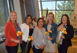 Cinco mujeres posan para la foto con flores en la mano.