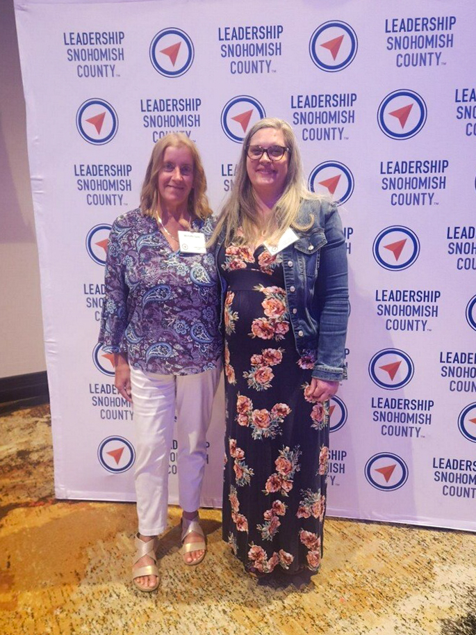 Two women pose in front of backdrop with Leadership Snohomish County logo. 