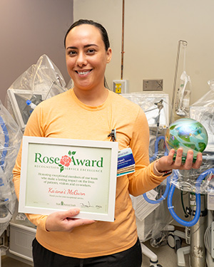 Woman in orange long sleeve top holds up Rose Award certificate and glass award.