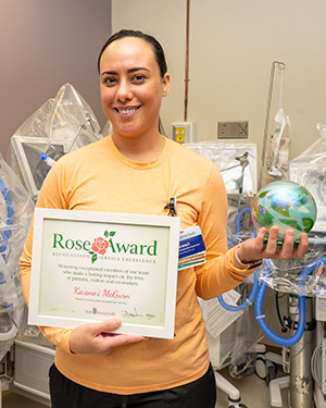 Mujer con una camiseta naranja de mangas largas sostiene el certificado del premio Rose Award y una esfera de vidrio.