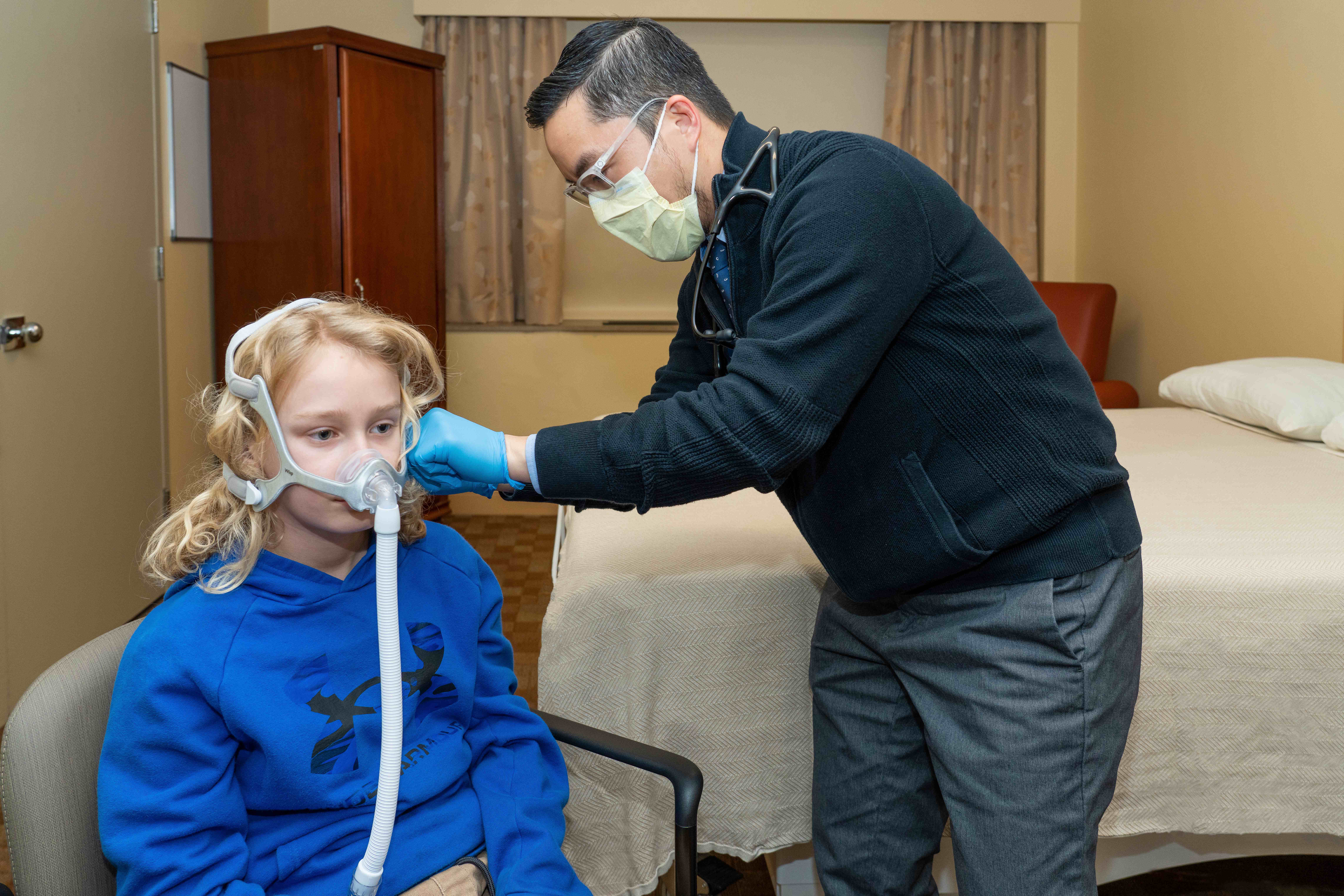 Male doctor helps boy patient put on CPAP machine.