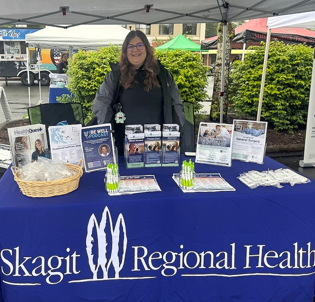 Woman stands behind Skagit Regional Health table topped with brochures, flyers and other giveaways.