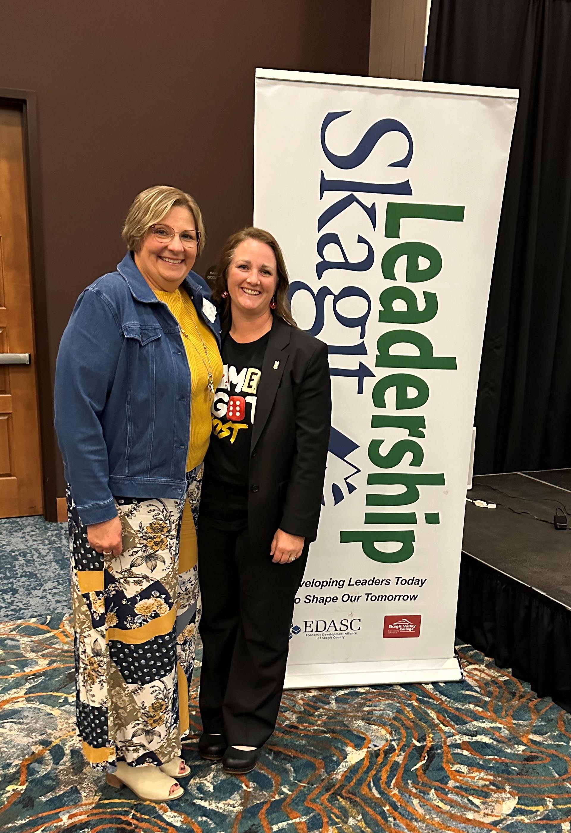 Two women standing by promotional banner at event