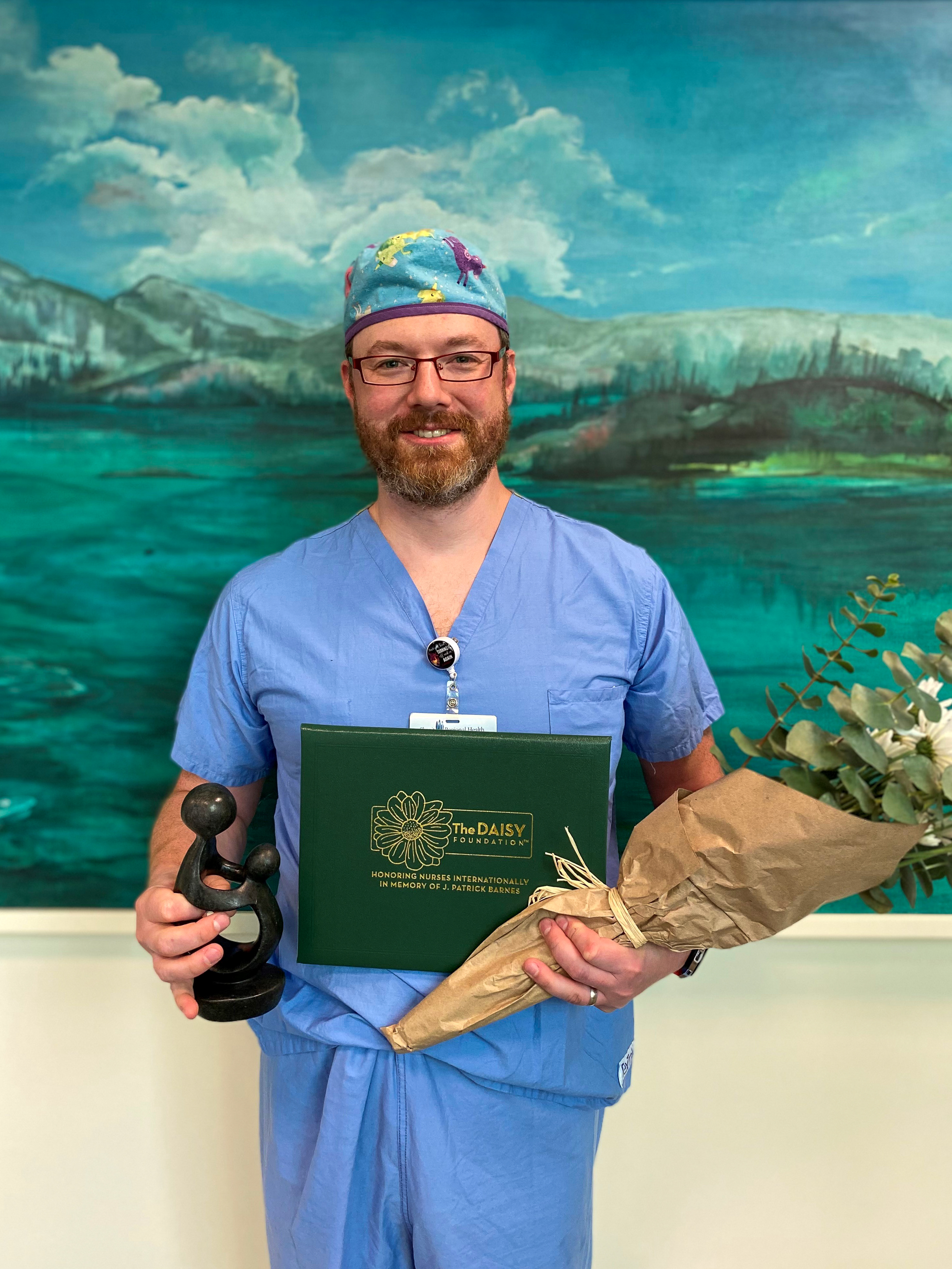 Wolfgang Stufflebeam holds DAISY award and bouquet of flowers.